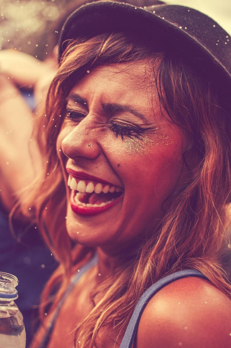 Smiling woman enjoying a fun nightclub party, wearing glitter and trendy hat.